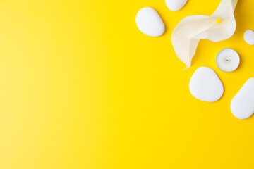 Spa background with white stones, candles and white flower on yellow. Flat lay,copy space