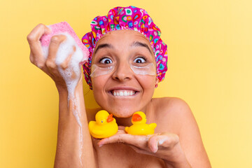 Young mixed race woman with shower cap holding a sponge and rubber ducks isolated on yellow background