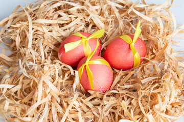 Decorated red Easter eggs lie in a nest made of wood shavings on a white background close-up.