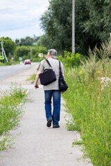 a man with bags in his hand is walking along a city road in the middle of a green forest