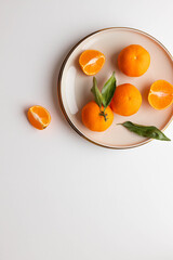 Fresh tangerine or clementin fruits on a beige plate with gold rim on a white background. Colorful fruit background. Flat lay, top view, copy space