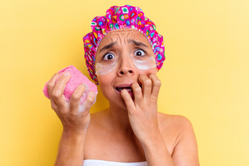 Young mixed race woman taking a bath holding a sponge bath with a dark circle patches isolated biting fingernails, nervous and very anxious.