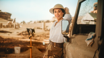 Portrait of Beautiful Female Adventurer Standing Near Off-Road Car. Stylish Great Archaeologist Posing, Looking at Camera. In Background Ancient Civilization City, Fossil Remains Archeological Site - obrazy, fototapety, plakaty