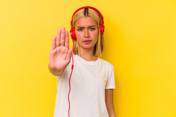 Young venezuelan woman listening music isolated on yellow background standing with outstretched hand showing stop sign, preventing you.