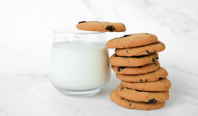 Stack of freshly baked homemade chocolate chip cookies and glass of milk on marble background. Recipe of home bakery, cookies with chocolate chips.