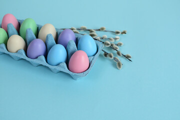 colorful eggs in a blue cardboard tray and willow bouquet. Easter decorations. Easter egg. Spring composition.