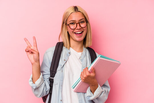 Young venezuelan student woman isolated on pink background joyful and carefree showing a peace symbol with fingers.