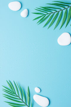 Spa background with white stones and palm leaves on blue. Flat lay,copy space