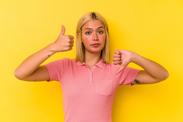 Young venezuelan woman isolated on yellow background showing thumbs up and thumbs down, difficult choose concept