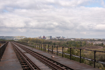 Railway tracks on a bridge, view of an industrial area under a cloudy sky