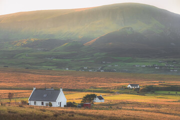 Golden sunset or sunrise light over rural countryside landscape of Staffin village and white croft houses with the Quiraing and Trotternish Ridge on the Isle of Skye, Scotland.