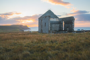 Old, ancient stone ruins of the remote and isolated Kilmuir Church in the seaside Scottish rural countryside at sunset or sunrise on the Isle of Skye, Scotland.