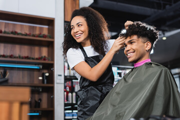 Cheerful african american hairstylist and client looking away in salon - Powered by Adobe