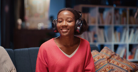 Obraz premium Young afro-american woman lies on couch connecting to friends videochat communicating about lifestyle drinking hot tea relaxing at home.
