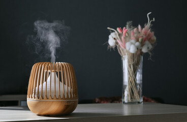 Stylish aroma oil diffuser on the background of a vase of flowers. Comfortable home environment.