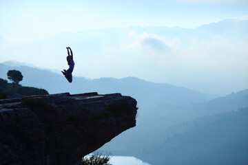 Woman jumping in a cliff on blue landscape
