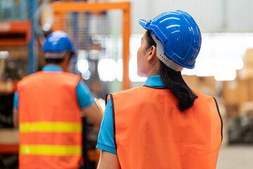Asian young female employee warehouse worker with safety vest and helmet using clipboard for...