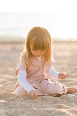 Fototapeta na wymiar Pretty little child 2-3 year old playing at beach over sea at background in sun light outdoors. Small kid wearing summer clothes outside. Vacation season. Childhood.