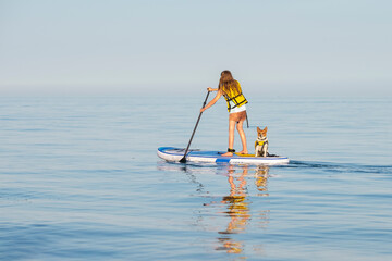 Young teenage girl in a life vest paddle boarding on a stand up board with a pet dog at Lake...