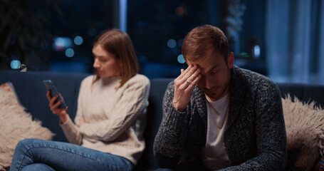 Obraz premium Caucasian young married couple making up conflict in their apartment. Angry young woman fell jealous about her husband reading messages on his smartphone.