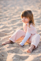 Pretty little child 2-3 year old playing at beach over sea at background in sun light outdoors. Small kid wearing summer clothes outside. Vacation season. Childhood.
