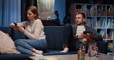 Family in Conflict. Young Caucasian Sad Couple of Wife and Husband Using Smartphones Separating from Each Other. Living Room. Apartment. Relationship problems.