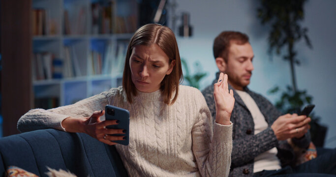 Angry caucasian sad young man and woman making up quarrel in their apartment. Emotional negative couple agruing and using mobile phones separately.
