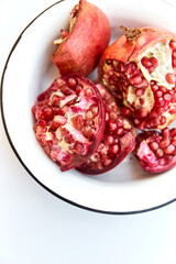 Craked ripe pomegranate and garnet seeds in metall bowl on white desk with place for text. Garnet background. Vegetarian Concept, Organic Vitamins