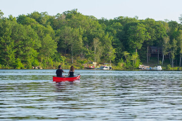 A couple enjoying a trip in a red wooden canoe on the lake on warm sunny day. Selective focus.