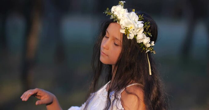 Close-up portrait of a Caucasian teenager girl with long brown hair and blue eyes in a flower wreath dancing and smiling on a nature background. 4k 50 fps slow motion