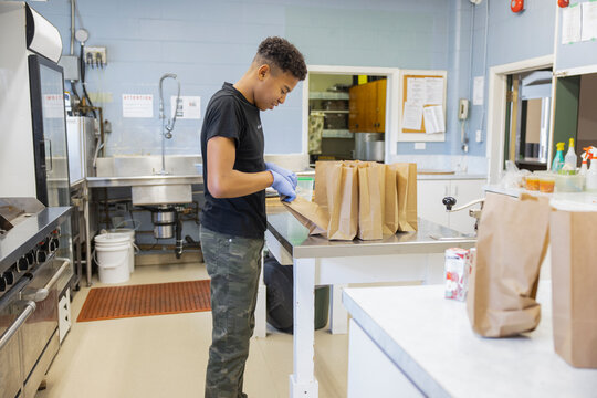 Teenage boy volunteer packing sack lunches in community center kitchen