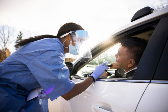 Nurse in PPE taking nasal swab test for man in car