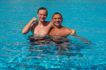 Real people concept, beautiful young man and teenage boy swimming and having fun in pool in vacation. happiness and nice body for enjoyed people lifestyle as vacation. Father hugging son.