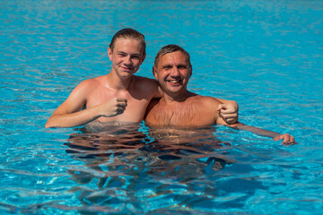 Fototapeta premium Real people concept, beautiful young man and teenage boy swimming and having fun in pool in vacation. happiness and nice body for enjoyed people lifestyle as vacation. Father hugging son.