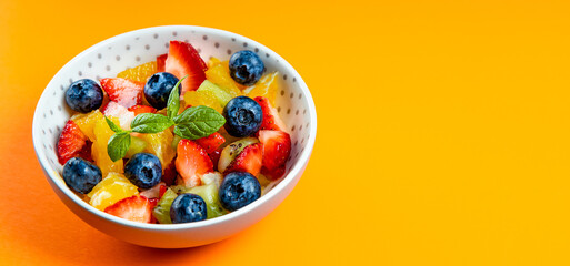 Web banner with fresh summer salad of various fruits and berries. Kiwi, orange, strawberry and blueberry on a plate decorated with mint on an orange background