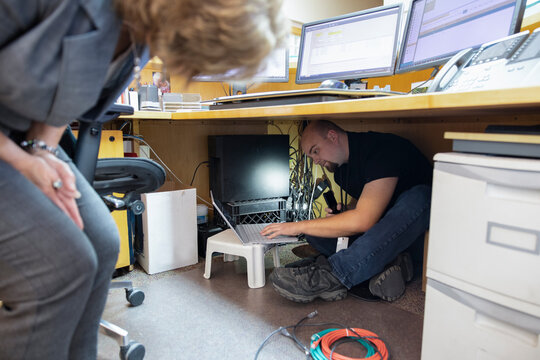 Technician Fixing Wiring Under Desk In Office