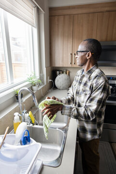 Senior Man Drying Hands At Kitchen Sink, Looking Out Window