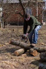 Preparing firewood for the winter, cherry logs piled in a heap in the yard, a farmer sawing a log...