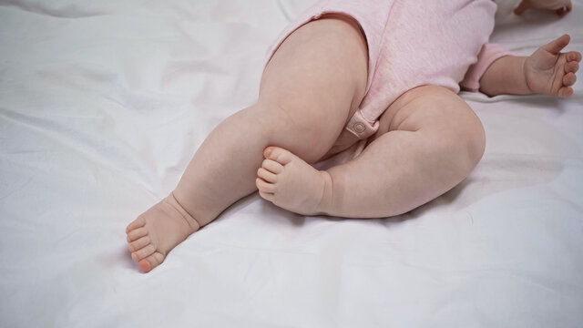 partial view of baby in romper with barefoot lying on bed.