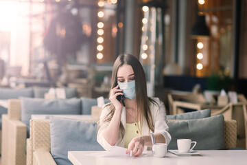 Female manager in a suit and medical mask works remotely on street cafe.