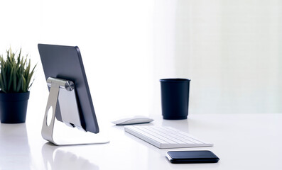 Creative workspace with tablet on stand holder, keyboard, mouse and black cup on white table.