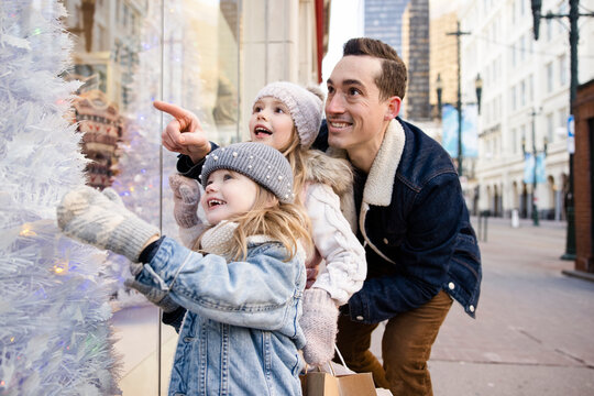 Father and daughters looking at Christmas tree window display in city