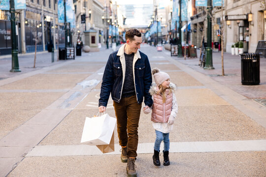 Father and daughter with shopping bags holding hands in winter city