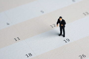 Selective focus miniature businessman standing on calendar checking schedule.