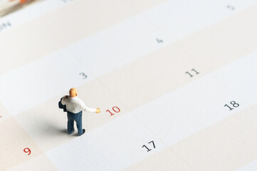 Selective focus miniature businessman standing on calendar checking schedule.