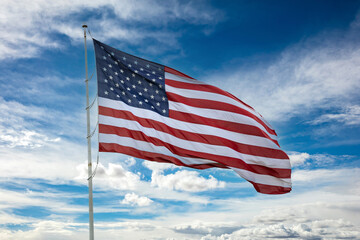 USA flag on a pole waving against blue cloudy sky background.