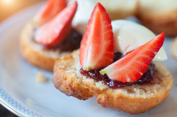 Close up strawberry scones with jam and whipped cream in white plate.