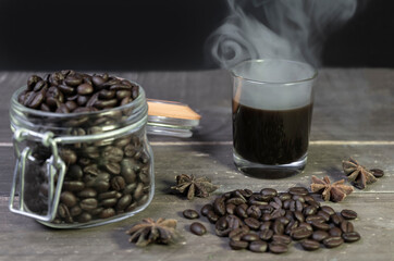 Hot american black coffee with smoke and coffee beans in glass jar on wooden table.Creative vintage closeup view dark background with copy space.