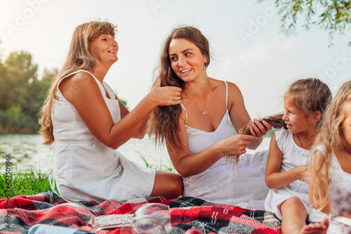 Mother's day. Mother, grandmother and daughter weaving hair braids to each other. Family having fun on picnic in park.