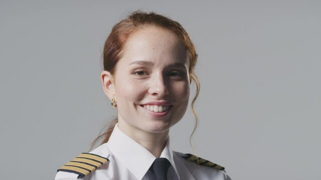 Smiling young female airline pilot or ship captain wearing uniform in front of plain studio background - shot in slow motion